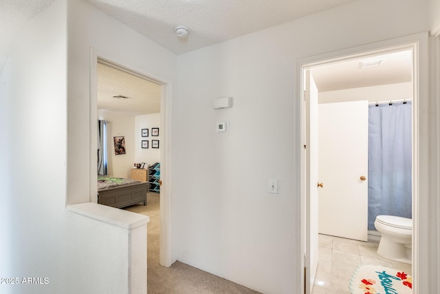 hallway with light colored carpet, a textured ceiling, and light tile patterned flooring