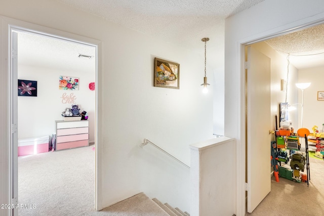 corridor with an upstairs landing, carpet floors, and a textured ceiling