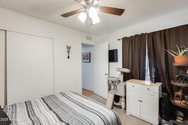 bedroom featuring visible vents, a ceiling fan, a textured ceiling, a closet, and light colored carpet