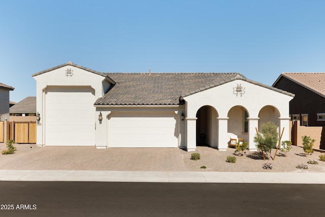 view of front facade featuring a tile roof, an attached garage, fence, decorative driveway, and stucco siding