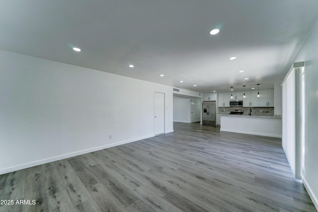 unfurnished living room with recessed lighting, wood finished floors, and baseboards
