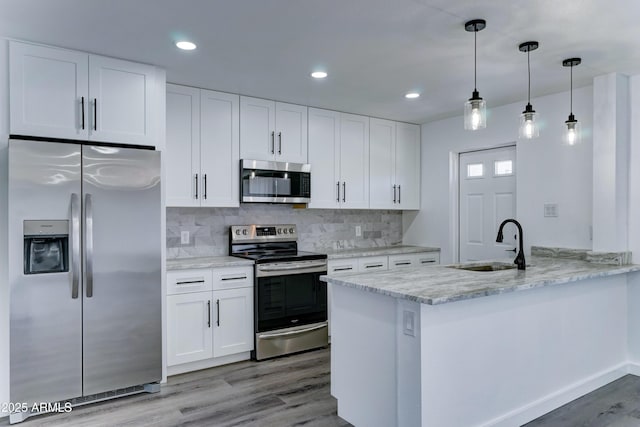 kitchen with appliances with stainless steel finishes, a sink, white cabinets, a peninsula, and light wood-style flooring