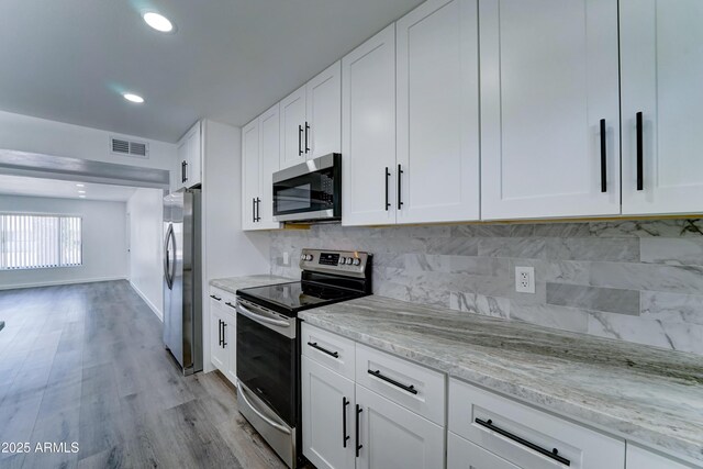kitchen with appliances with stainless steel finishes, light stone counters, light wood-style floors, tasteful backsplash, and recessed lighting
