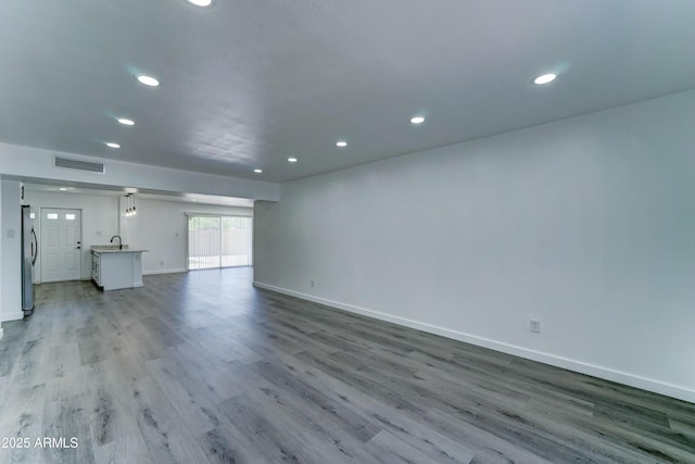 unfurnished living room with recessed lighting, baseboards, wood finished floors, and a sink