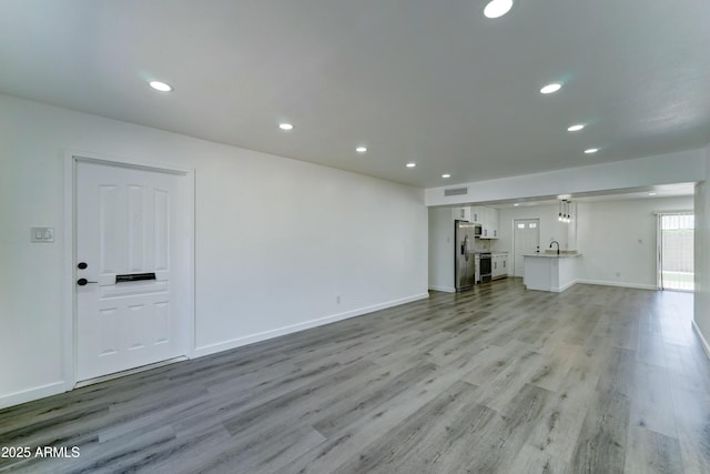 unfurnished living room with light wood-type flooring, recessed lighting, baseboards, and a sink