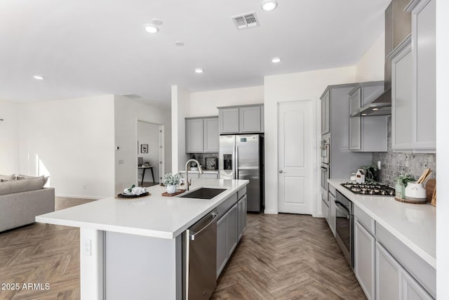 kitchen featuring sink, gray cabinets, appliances with stainless steel finishes, a center island with sink, and parquet floors