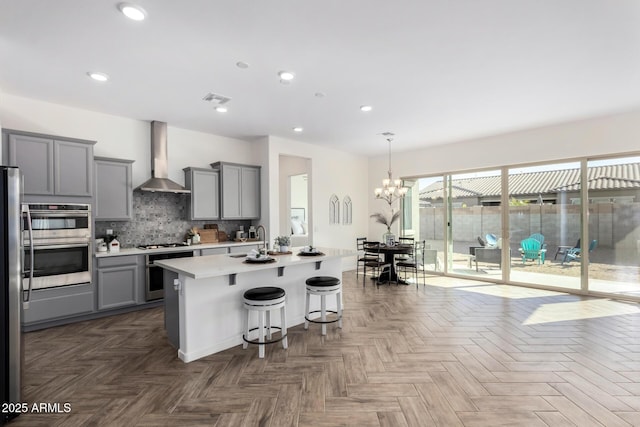 kitchen with wall chimney exhaust hood, a center island with sink, gray cabinets, dark parquet floors, and stainless steel appliances