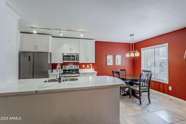 kitchen featuring light stone counters, a sink, stainless steel appliances, white cabinets, and decorative light fixtures