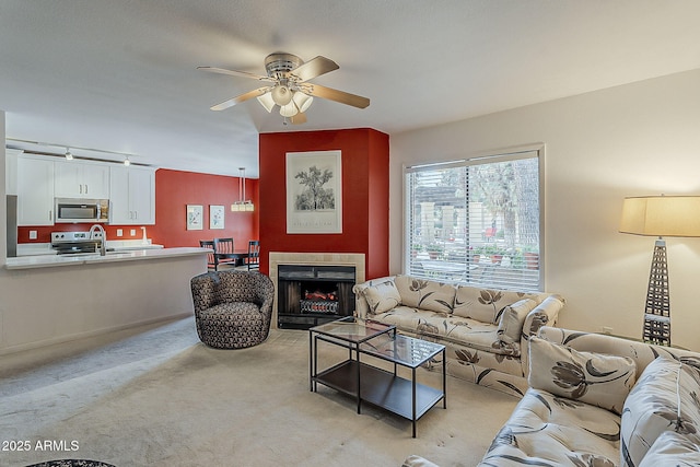 living area featuring track lighting, a fireplace, light colored carpet, and ceiling fan