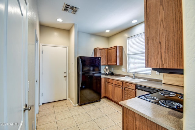 kitchen featuring sink, light tile patterned floors, black refrigerator, stainless steel dishwasher, and cooktop