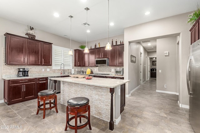 kitchen featuring stainless steel appliances, a center island, a kitchen breakfast bar, tasteful backsplash, and decorative light fixtures