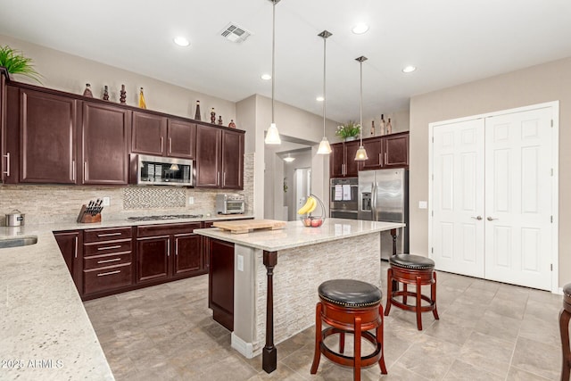 kitchen with appliances with stainless steel finishes, decorative light fixtures, a breakfast bar area, a center island, and light stone countertops