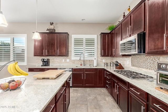 kitchen with light stone counters, sink, decorative light fixtures, and stainless steel appliances