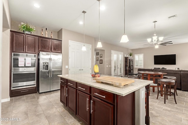 kitchen with appliances with stainless steel finishes, pendant lighting, a center island, a notable chandelier, and light stone countertops