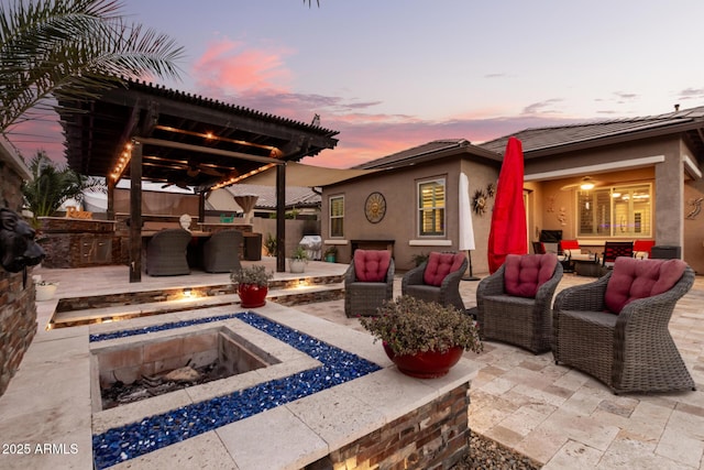 patio terrace at dusk with exterior kitchen and an outdoor living space with a fire pit