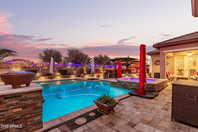 pool at dusk with an in ground hot tub and a patio area