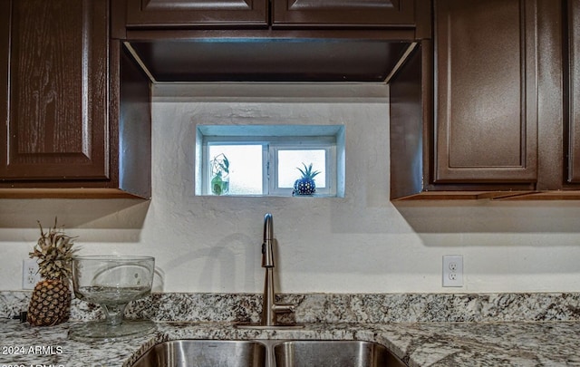 details with dark brown cabinetry, light stone counters, and sink