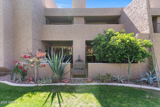 property entrance with stucco siding, a lawn, a gate, fence, and a balcony