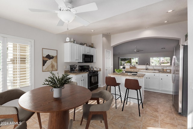 kitchen with light stone counters, a kitchen island, sink, black appliances, and white cabinetry