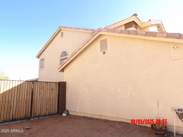 view of side of property with a gate, stucco siding, and fence