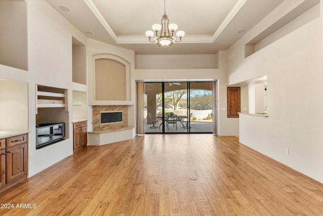 unfurnished living room with a raised ceiling, a premium fireplace, light wood-type flooring, a towering ceiling, and a notable chandelier