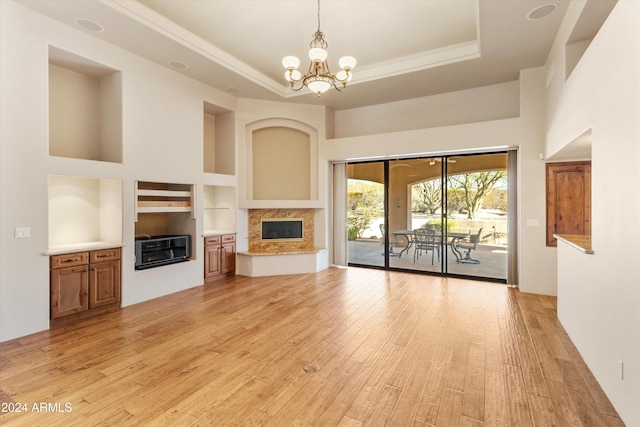 unfurnished living room with built in features, a high end fireplace, a chandelier, a tray ceiling, and light wood-type flooring