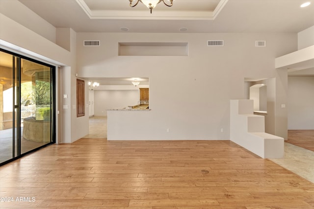 unfurnished living room featuring a raised ceiling, light wood-type flooring, a towering ceiling, and an inviting chandelier