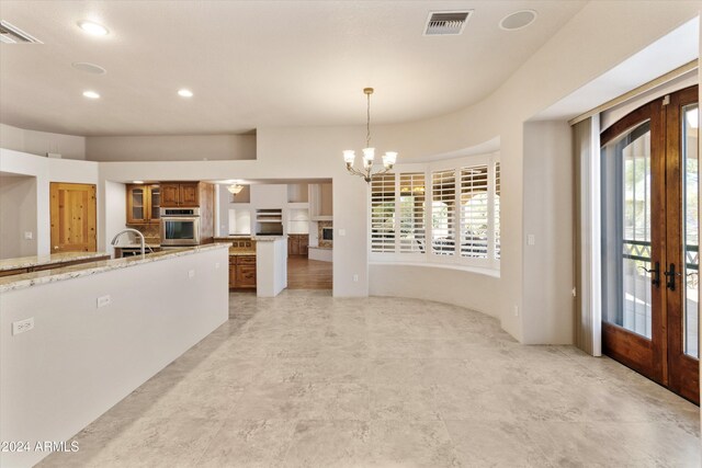 kitchen featuring light stone countertops, french doors, decorative light fixtures, a notable chandelier, and oven