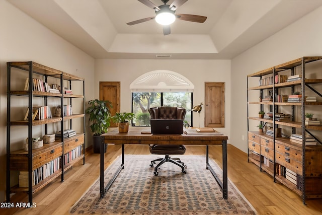 office area featuring a tray ceiling, ceiling fan, and light wood-type flooring