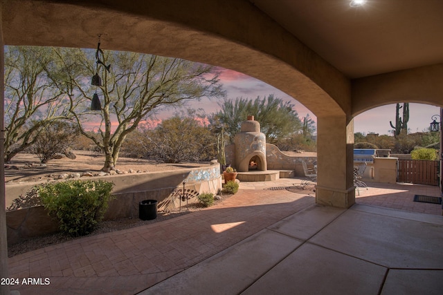 patio terrace at dusk featuring an outdoor stone fireplace and area for grilling