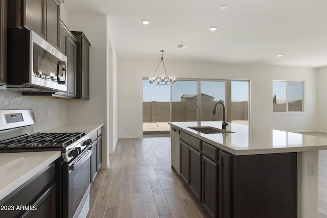 kitchen with sink, light hardwood / wood-style flooring, appliances with stainless steel finishes, tasteful backsplash, and a center island with sink