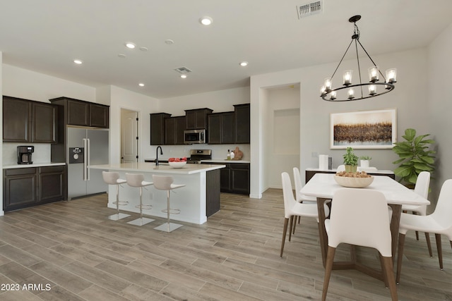 kitchen featuring decorative light fixtures, an island with sink, sink, light hardwood / wood-style floors, and stainless steel appliances