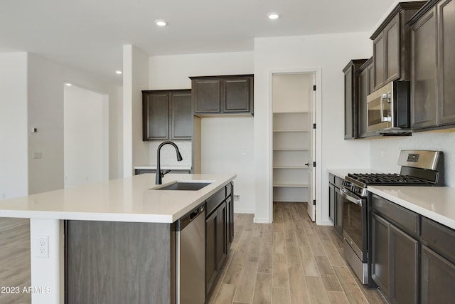 kitchen featuring dark brown cabinetry, sink, an island with sink, stainless steel appliances, and light hardwood / wood-style floors