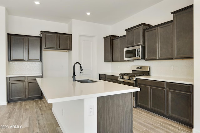 kitchen featuring sink, a kitchen island with sink, backsplash, dark brown cabinets, and stainless steel appliances