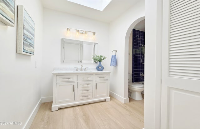 bathroom featuring vanity, tiled shower, toilet, hardwood / wood-style flooring, and a skylight