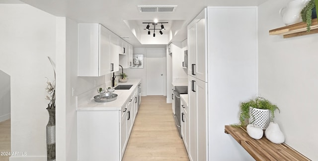 kitchen with a raised ceiling, stainless steel electric range oven, white cabinets, and light hardwood / wood-style floors