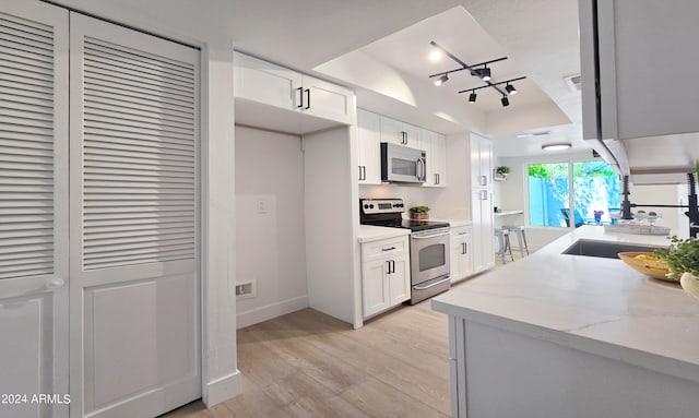 kitchen with appliances with stainless steel finishes, white cabinetry, light stone counters, light wood-type flooring, and track lighting