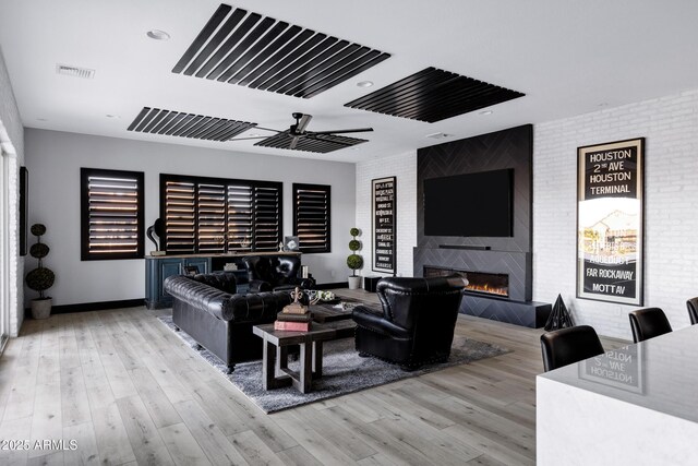 living area with visible vents, wood finished floors, a fireplace, and brick wall