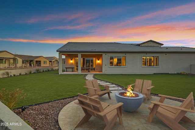 back of property at dusk with stucco siding, a fire pit, a lawn, and a patio