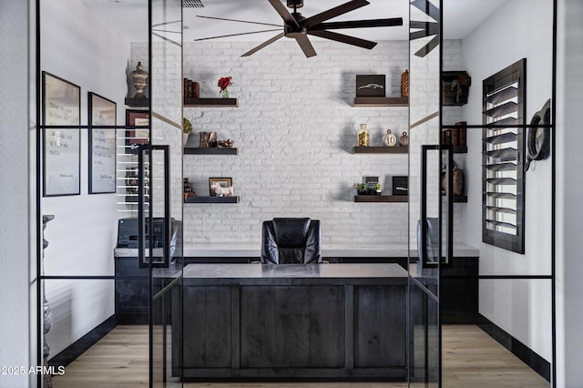 office area featuring baseboards, a ceiling fan, light wood-style floors, and brick wall