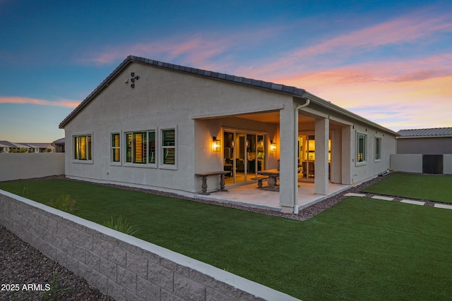 rear view of house with a lawn, a patio, stucco siding, and a fenced backyard