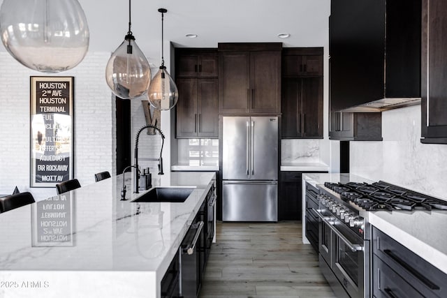 kitchen with tasteful backsplash, hanging light fixtures, light stone counters, a sink, and premium appliances