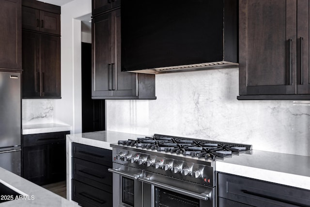 kitchen with dark brown cabinets, backsplash, wall chimney exhaust hood, and appliances with stainless steel finishes