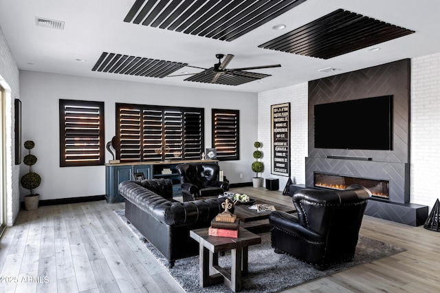 living area featuring a large fireplace, ceiling fan, visible vents, baseboards, and wood finished floors