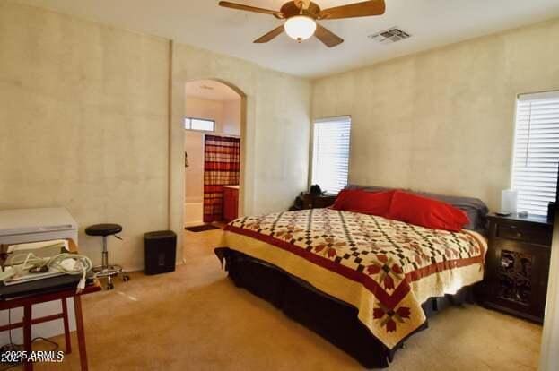 bedroom featuring carpet, visible vents, a ceiling fan, arched walkways, and ensuite bathroom