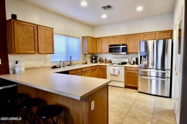 kitchen with visible vents, brown cabinets, a sink, appliances with stainless steel finishes, and a peninsula