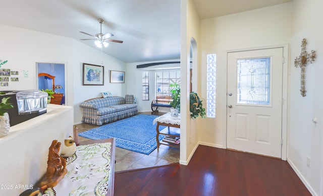 foyer featuring a ceiling fan, arched walkways, vaulted ceiling, wood finished floors, and baseboards