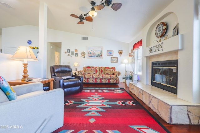 living area featuring a ceiling fan, vaulted ceiling, a glass covered fireplace, and visible vents