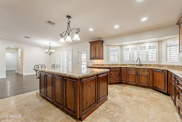 kitchen featuring sink, light hardwood / wood-style flooring, hanging light fixtures, light stone countertops, and a kitchen island