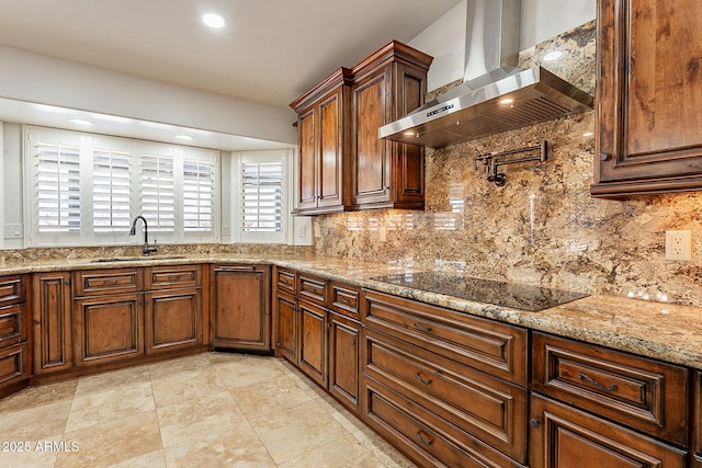 kitchen with wall chimney exhaust hood, sink, tasteful backsplash, black electric cooktop, and light stone countertops